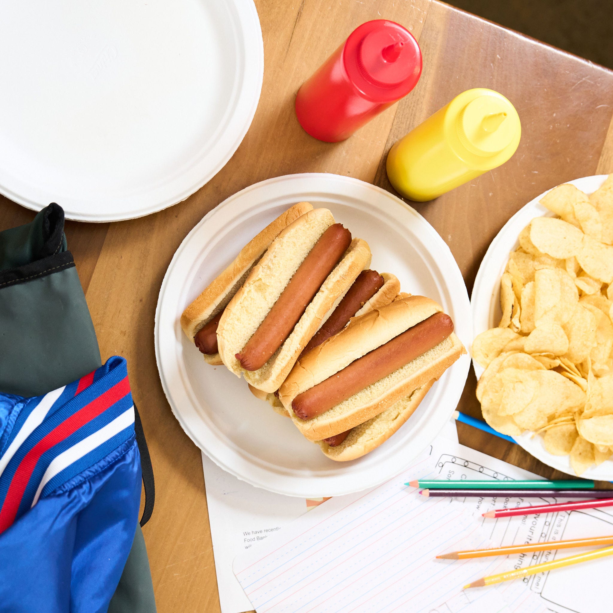 Hotdogs on a paper plate with mustard, ketchup and potato chips